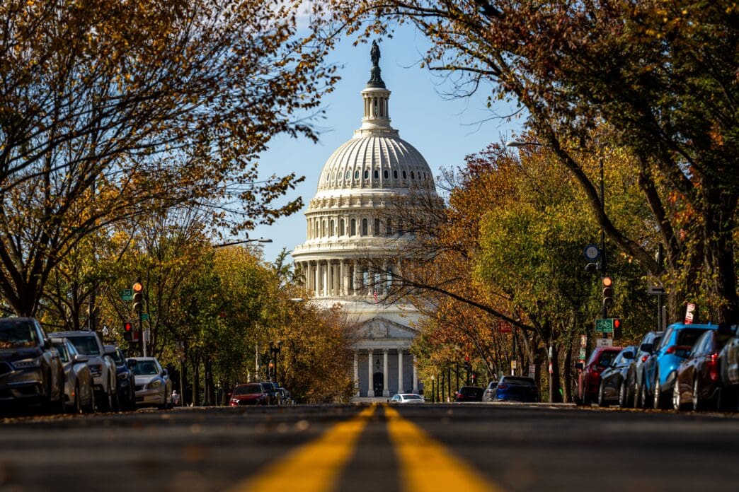 The US Capitol Building framed by autumn trees and a street with parked cars in Washington DC