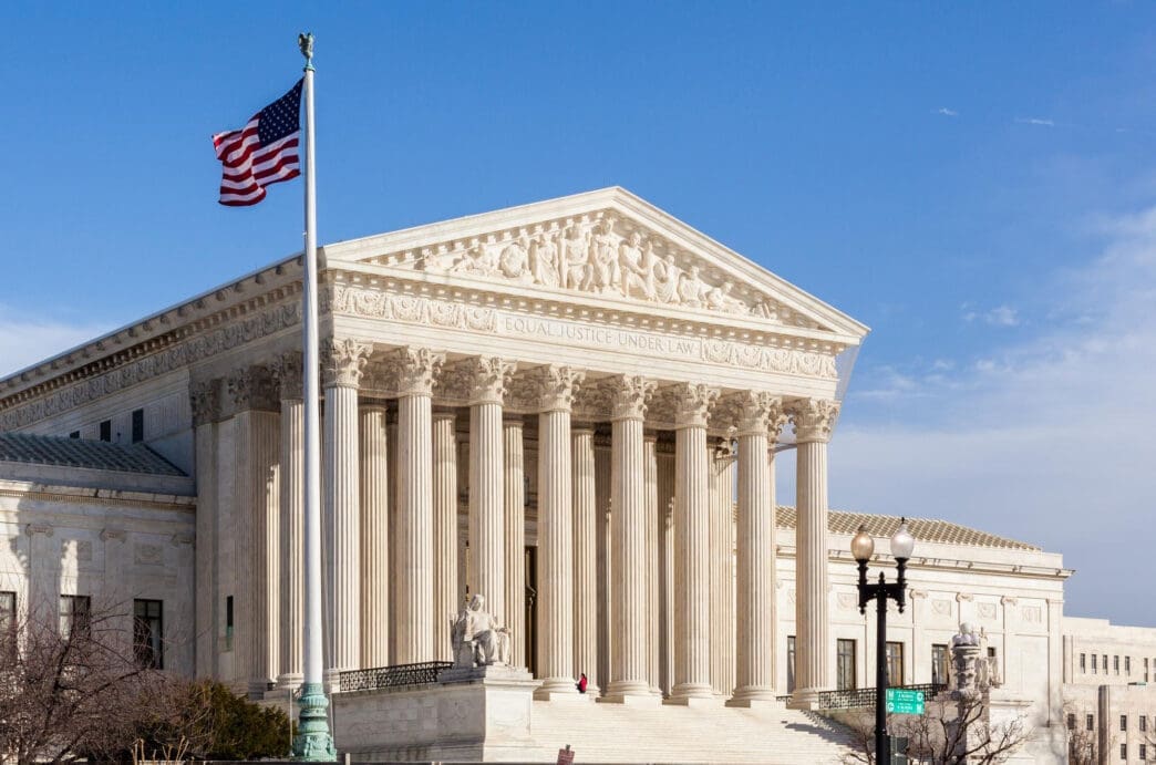 A medium shot of the US Supreme Court building facade, with the American flag waving.