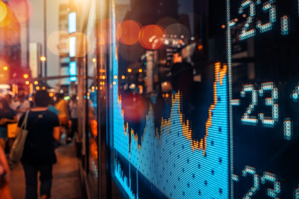 A digital stock market graph overlaid on a busy city street at night with bright bokeh lights.