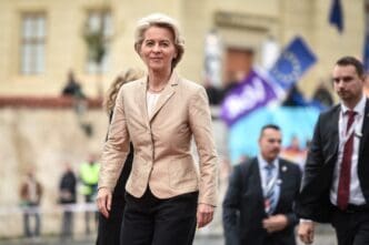 Ursula von der Leyen walks forward, smiling, with security personnel behind her.