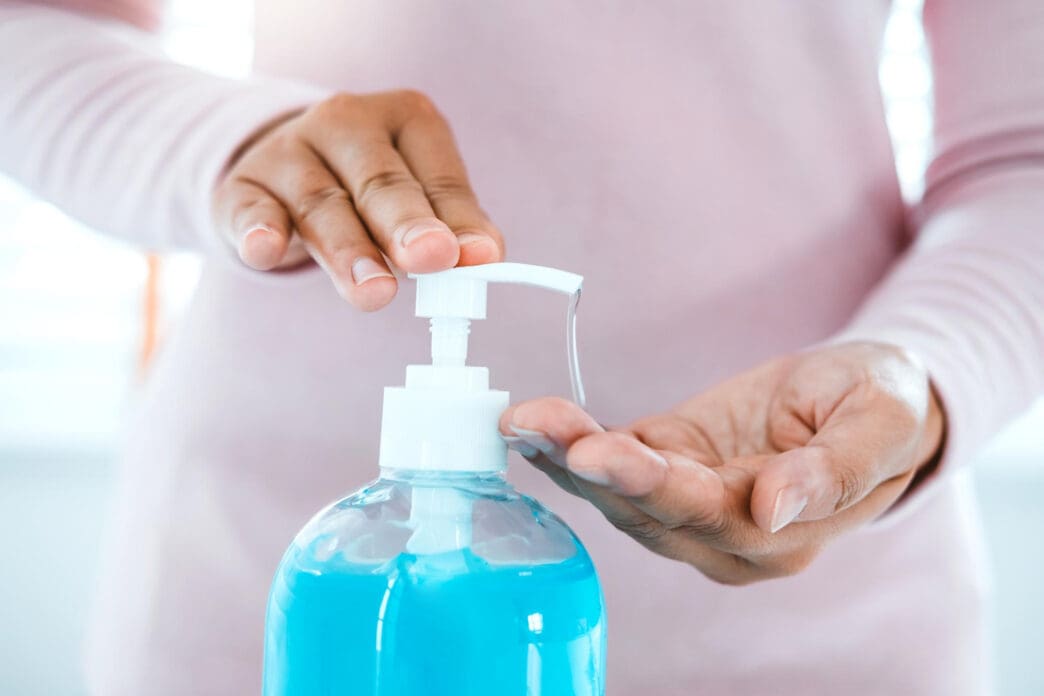 A person dispenses blue hand sanitizer from a pump bottle into their cupped hand to practice good hygiene.