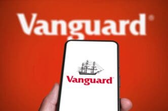 A smartphone displays the Vanguard logo, held in front of a larger, out-of-focus version of the same logo on a red background.