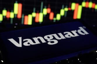 The Vanguard logo on a smartphone screen displayed against a blurred stock market candlestick chart.