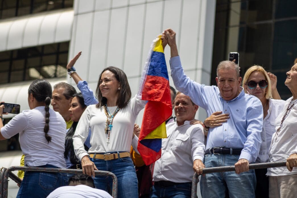 Venezuelan opposition leaders Maria Corina Machado and Edmundo González Urrutia wave the national flag at a rally, surrounded by supporters.