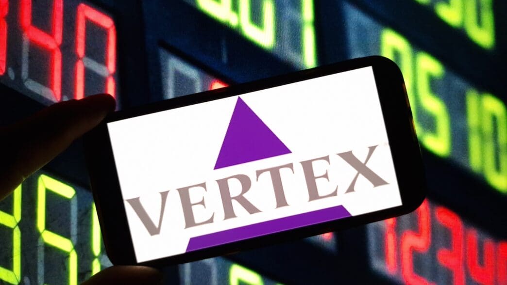 The Vertex Pharmaceuticals logo is displayed on a smartphone held against a colorful, digital stock market ticker.