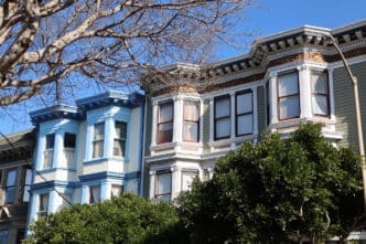 Row of ornate, Victorian-style townhouses with bay windows, under a clear blue sky.