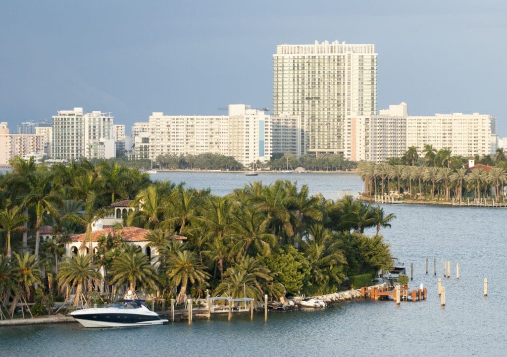 A luxury yacht is docked at a waterfront home on Star Island, with the modern Miami Beach skyline visible across the bay.