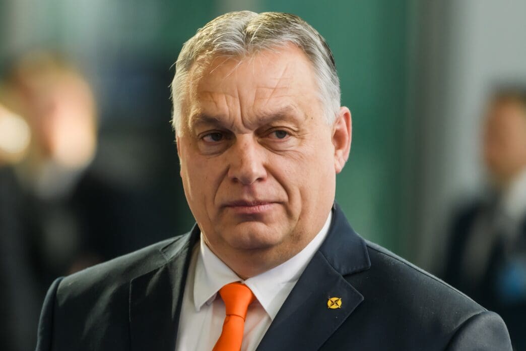 Hungarian Prime Minister Viktor Orbán, wearing a dark suit and orange tie, looks forward at a press event in Brussels.