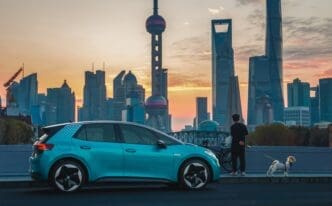 A turquoise Volkswagen ID.3 electric car parked in front of the Shanghai skyline and Oriental Pearl Tower at dawn