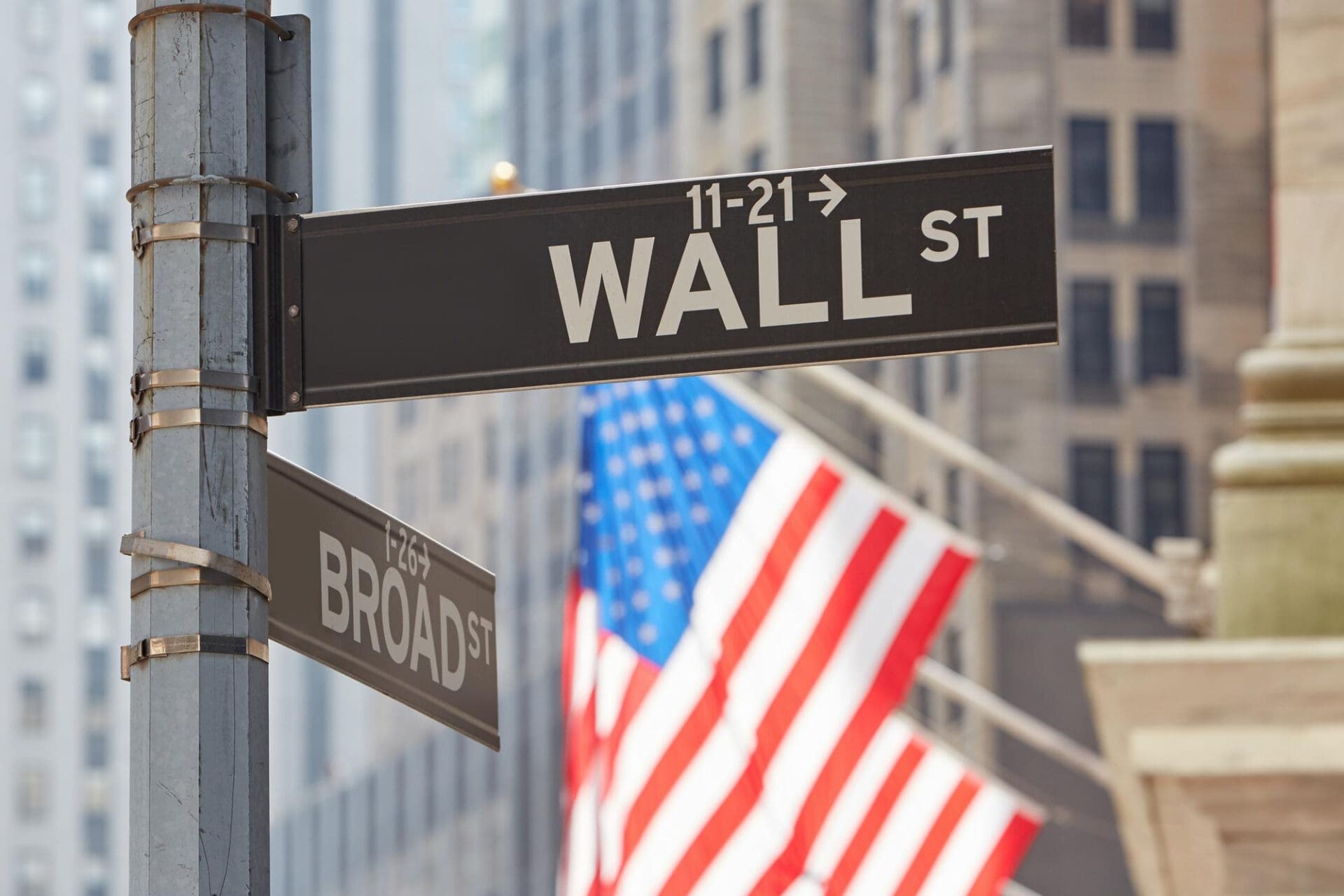 A close-up of the Wall Street street sign with an American flag and buildings blurred.