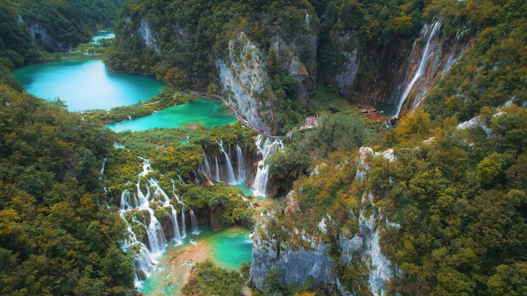 A high-angle view of the famous Plitvice park in Croatia, with its turquoise lakes, cascading waterfalls, and lush autumn forests.