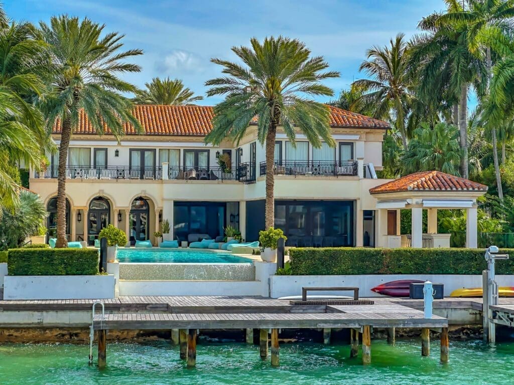 A luxury waterfront mansion on Miami's Star Island, featuring a pool, private dock, and surrounded by tall palm trees.