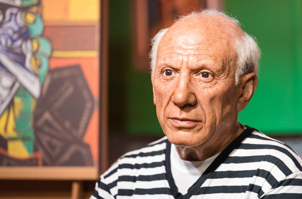 Close-up of a wax figure of artist Pablo Picasso, with an intense gaze, wearing a black and white striped shirt.