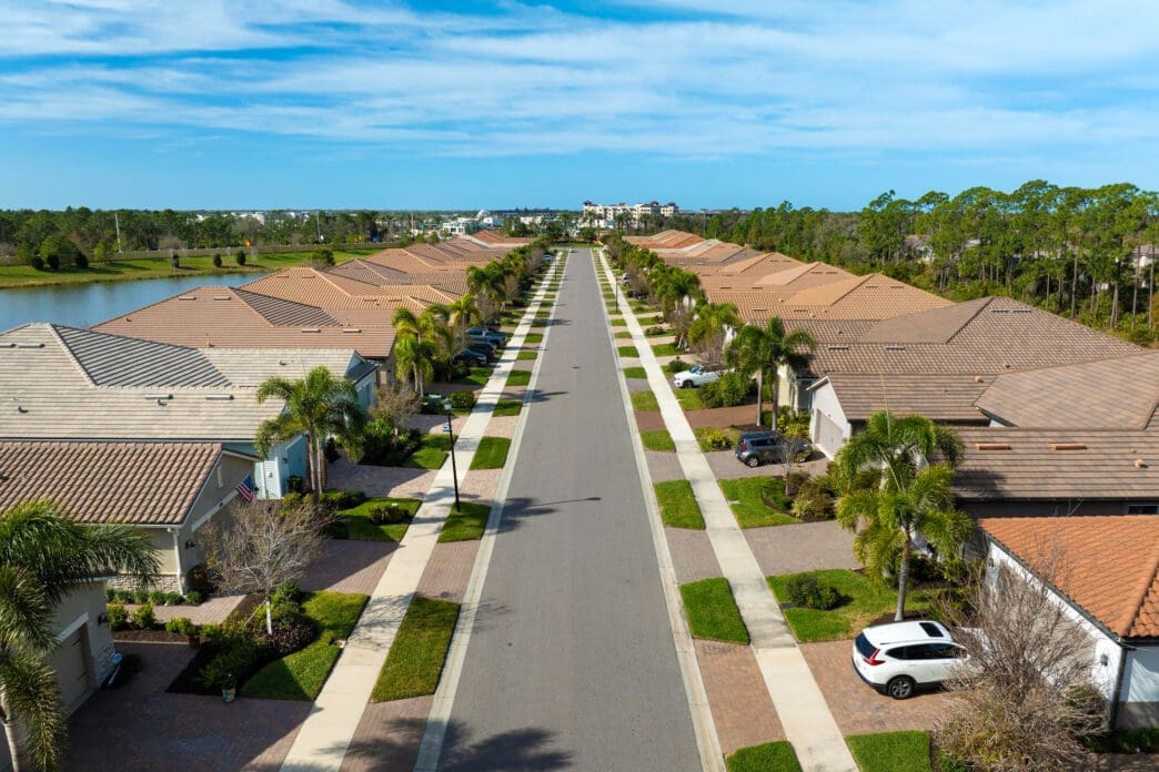 Aerial view of a straight suburban street lined with matching residential homes and palm trees in Florida.