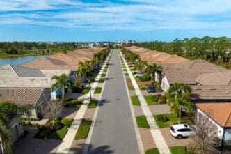 Aerial view of a straight suburban street lined with matching residential homes and palm trees in Florida.