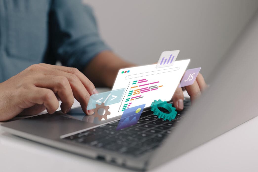 A developer types on a laptop, with holographic icons for code, JavaScript, and analytics floating above the keyboard.