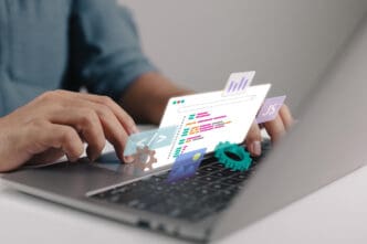 A developer types on a laptop, with holographic icons for code, JavaScript, and analytics floating above the keyboard.