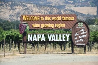 Large wooden sign welcoming visitors to the "world famous wine growing region" of Napa Valley, surrounded by vineyards and hills