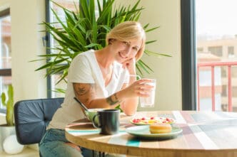 Woman with short blonde hair smiles while holding a glass of milk at a table with food