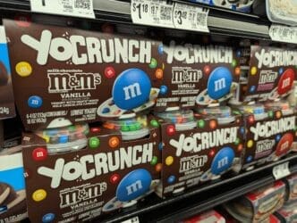 Boxes of YoCrunch Vanilla yogurt with M&M's toppings stacked on a refrigerated shelf at a grocery store