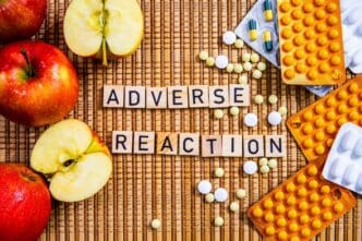 Close-up of apples spelling out the words "Adverse Reaction" next to pills and prescription drugs.