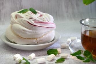 A white cake, a cup of tea, a white orchid, and mint leaves are arranged on a light background.