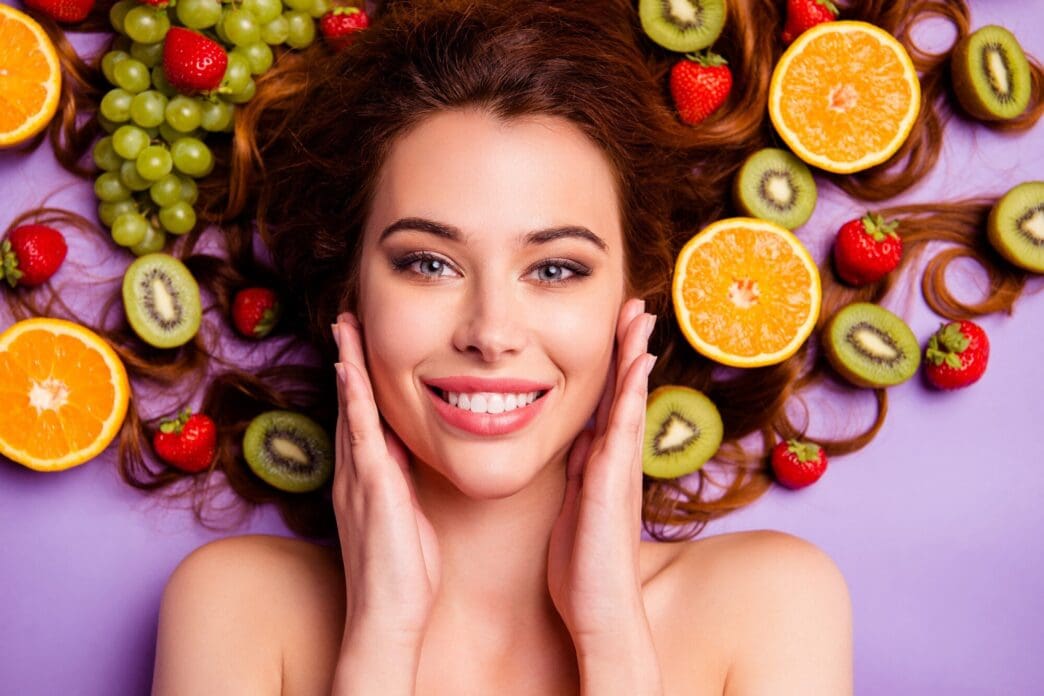 A redhead woman with fruits arranged in her hair poses for a portrait.