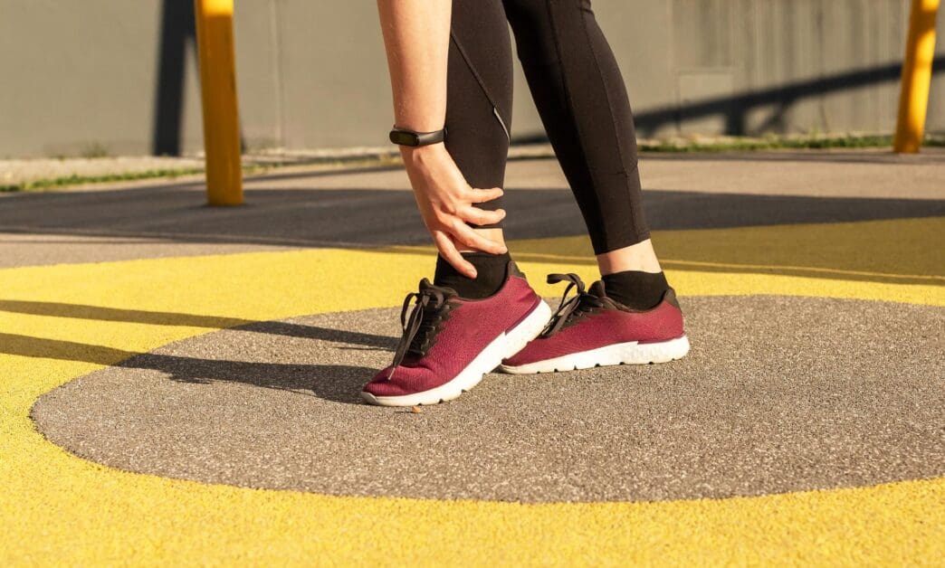A woman holds her painful foot, likely indicating a sports-related ankle injury.