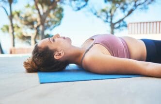A woman lies on a yoga mat outdoors, demonstrating a yoga pose for mindfulness and inner peace.