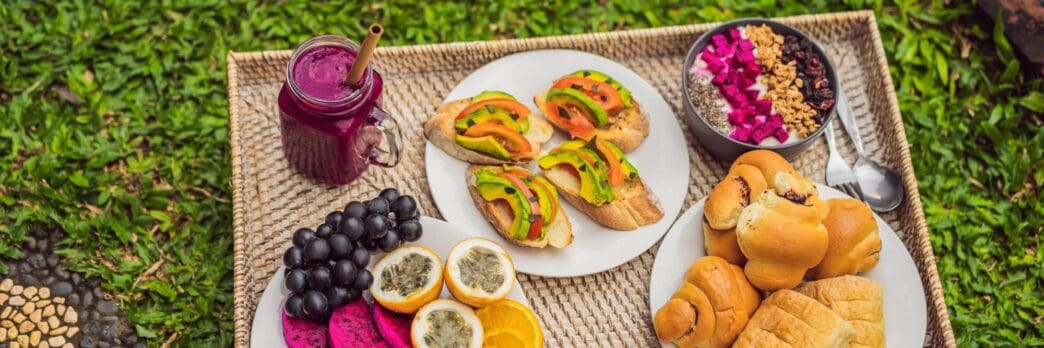 Breakfast tray with fruit buns, avocado sandwiches, and a smoothie bowl.