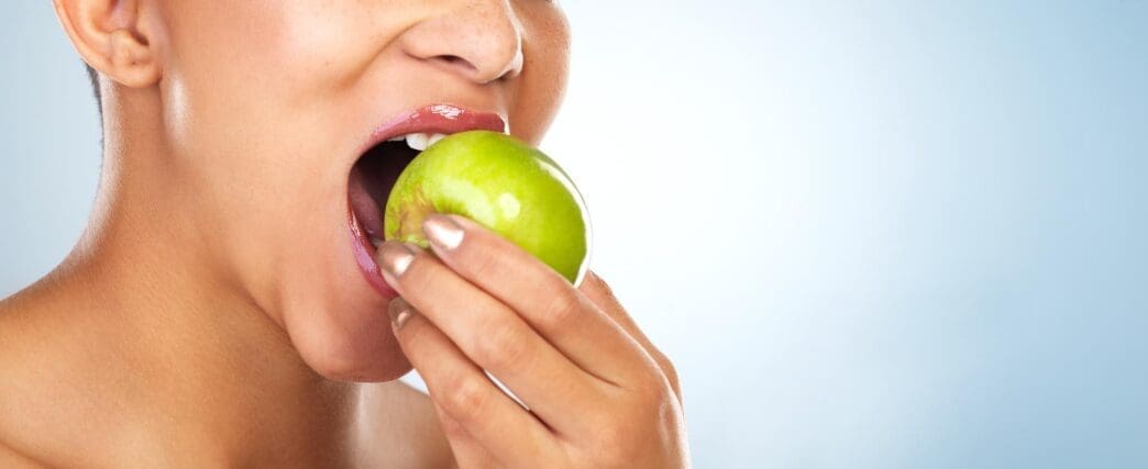 A woman takes a bite out of an apple, highlighting a healthy food choice against a blue background.