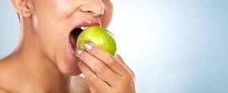 A woman takes a bite out of an apple, highlighting a healthy food choice against a blue background.