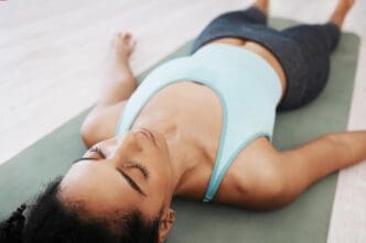 A Black woman meditates on a studio floor, promoting peace, calm, and wellness through prayer and yoga.