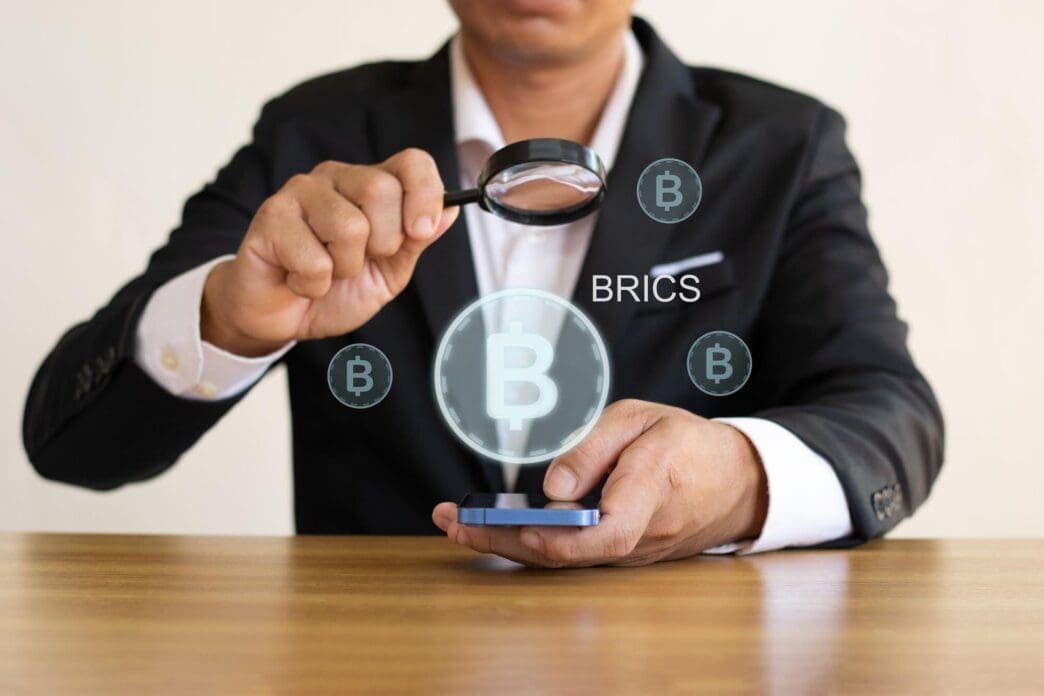 A graphic depicts the BRICS countries' flags surrounding a globe, illustrating their proposal for a new currency system for global trade.