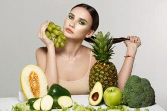A young brunette woman with makeup poses with various fruits.