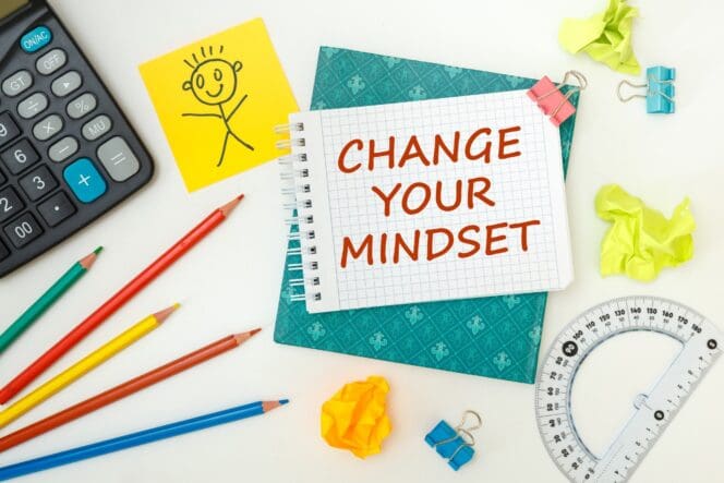 A notepad with the words "CHANGE YOUR MINDSET" is displayed on an office desk alongside office accessories.