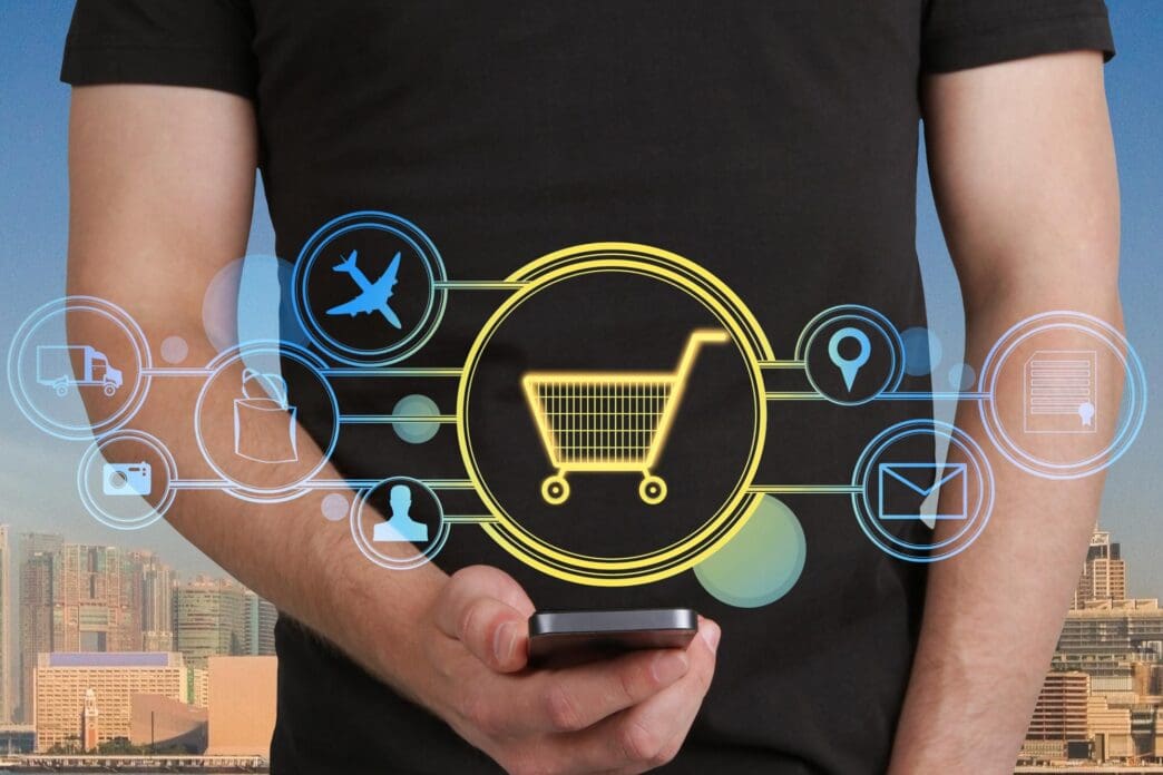 Close-up of a man's hand holding a smartphone with a glowing cart interface superimposed on a city background, illustrating online shopping.