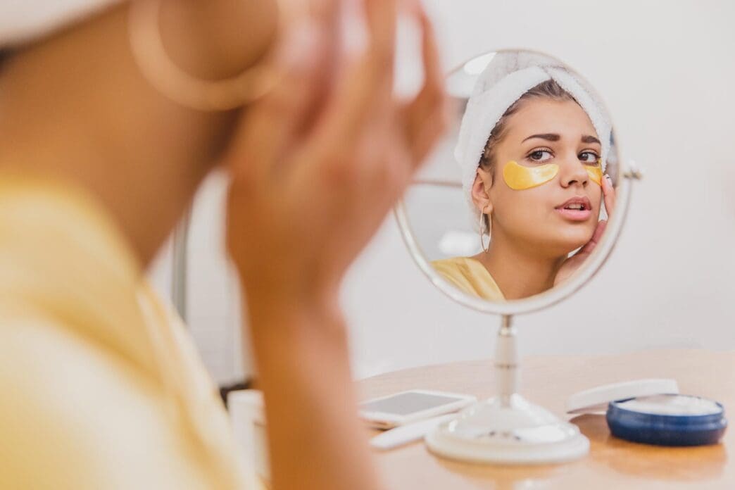 A woman with a towel on her head has under-eye patches applied.