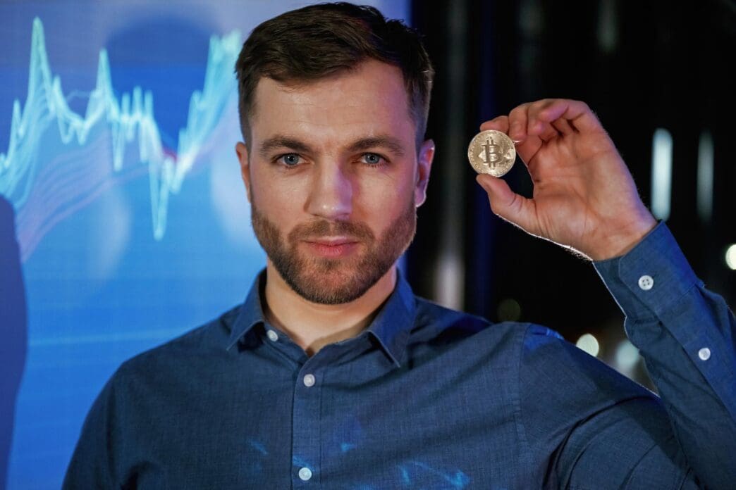 A person holds a digital currency coin in their hand while standing in front of a projector displaying data.