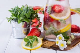 Close-up of a glass of homemade lemonade with strawberries and herbs, likely a detox soda water recipe.