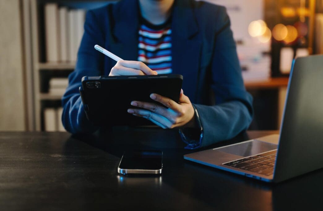 A businessman in a neon-lit office works on a laptop, tablet, and smartphone.