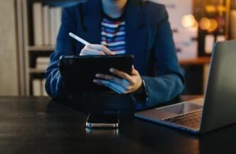 A businessman in a neon-lit office works on a laptop, tablet, and smartphone.
