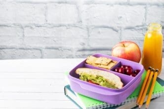 A healthy lunch box contains a sandwich, cookies, cherries, a bottle of juice, and an apple.