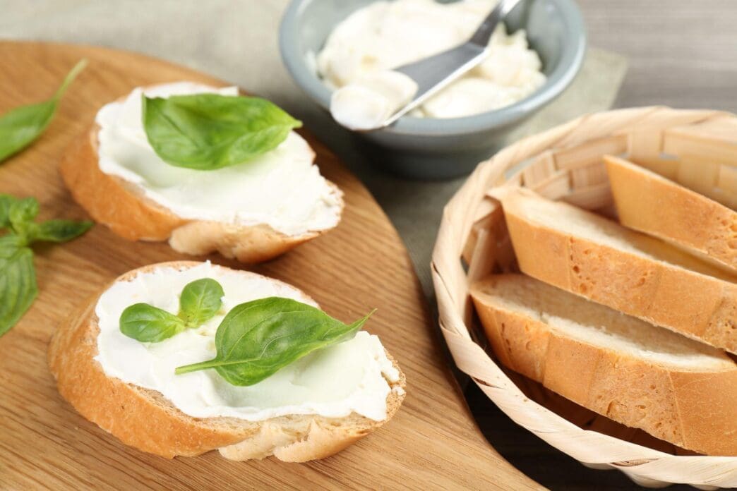 Close-up of sandwiches with cream cheese and basil leaves arranged on a wooden table.