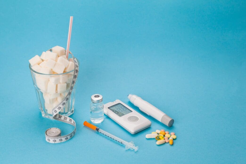 A medical concept image shows insulin syringes and pills next to a measuring tape and a glass filled with sugar cubes.