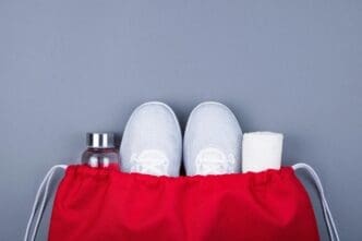 Overhead view of shoes, a towel, and a bottle inside a bag, set against a gray backdrop.
