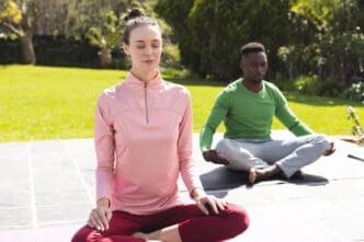 A diverse couple practices yoga and meditates together in a garden setting.