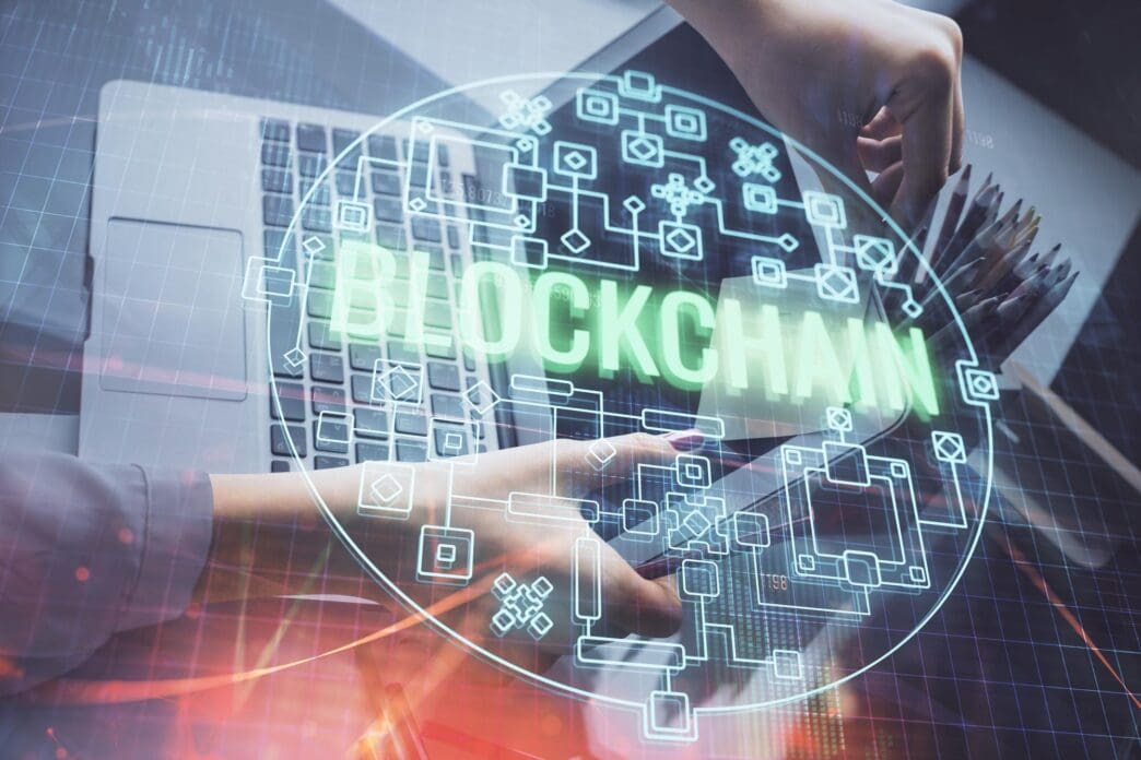 Double exposure image of a woman's hands typing on a computer keyboard overlaid with a holographic projection of a cryptocurrency market graph.