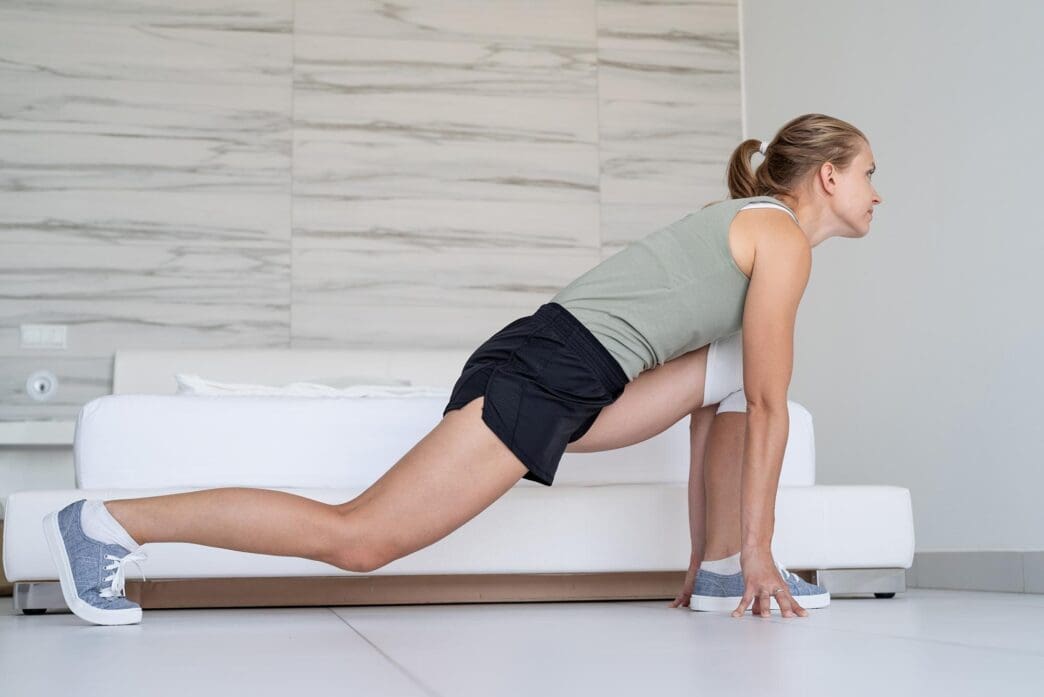 A smiling young woman does lunges in her bedroom as part of a home fitness and diet concept.