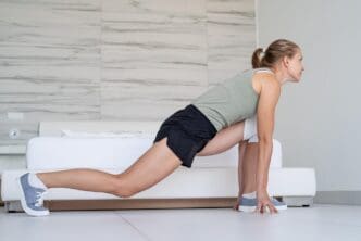 A smiling young woman does lunges in her bedroom as part of a home fitness and diet concept.